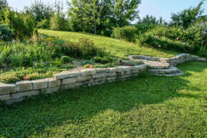 The image shows a sloping terrain of a garden. It implies that ground screws can be install in the most difficult of areas because in this case, it can level uneven ground.