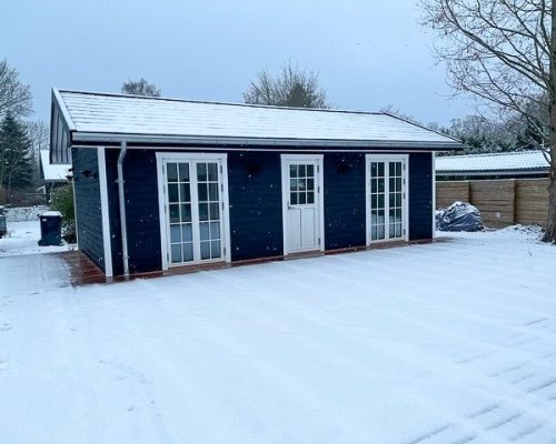 Dark-colored annex building with white doors and trim, surrounded by snow in a winter scene. Screw piles are a great garden room foundation.