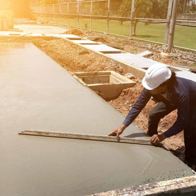 shutterstock_695743741-min-scaled-e1663844115673.jpg Person finishing wet concrete using a screeding tool on an outdoor construction project under bright sunlight.